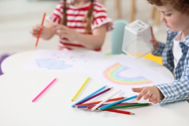 Little children drawing with colorful pencils at white table in kindergarten, closeup