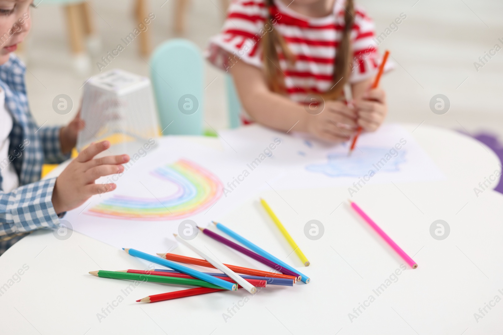 Photo of Little children drawing with colorful pencils at white table in kindergarten, closeup