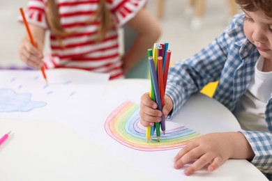 Photo of Little children drawing with colorful pencils at white table in kindergarten, closeup