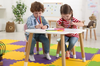Cute little children drawing with colorful pencils at white table in kindergarten