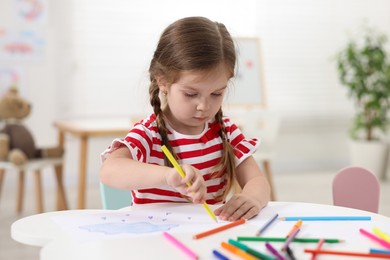 Cute little girl drawing at white table in kindergarten