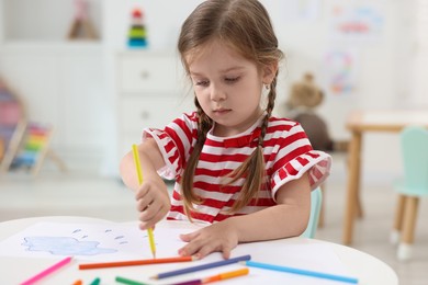 Photo of Cute little girl drawing at white table in kindergarten