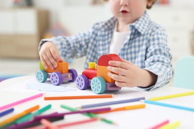 Photo of Little boy playing with toy cars at white table in kindergarten, closeup