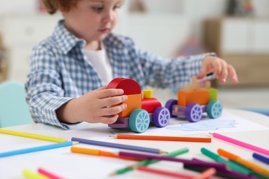 Little boy playing with toy cars at white table in kindergarten, closeup