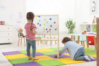 Photo of Little children learning alphabet with magnetic letters in kindergarten