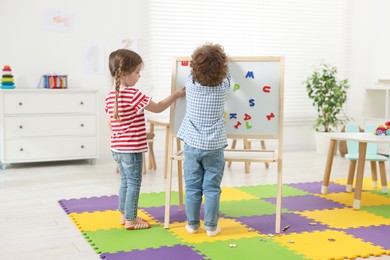 Cute little children learning alphabet with magnetic letters on board in kindergarten