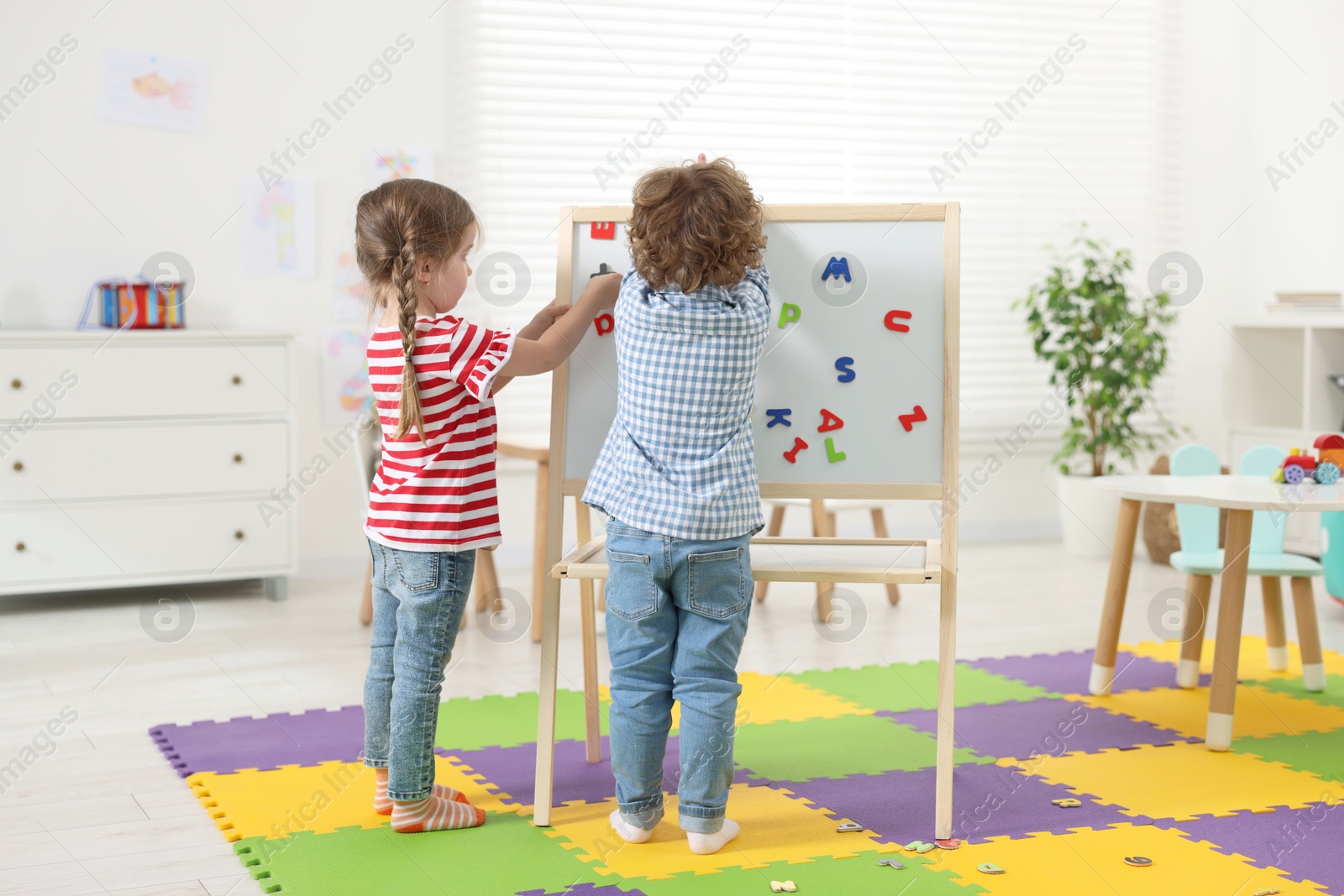 Photo of Cute little children learning alphabet with magnetic letters on board in kindergarten