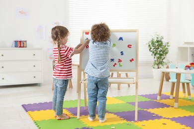 Photo of Cute little children learning alphabet with magnetic letters on board in kindergarten