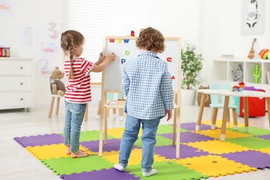 Photo of Cute little children learning alphabet with magnetic letters on board in kindergarten