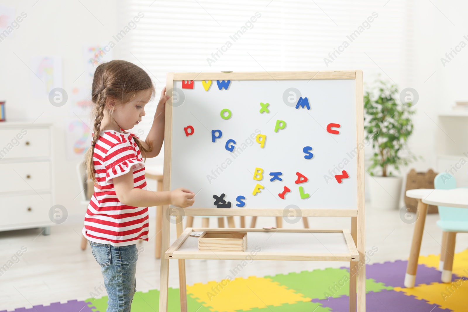 Photo of Little girl learning alphabet with magnetic letters in kindergarten