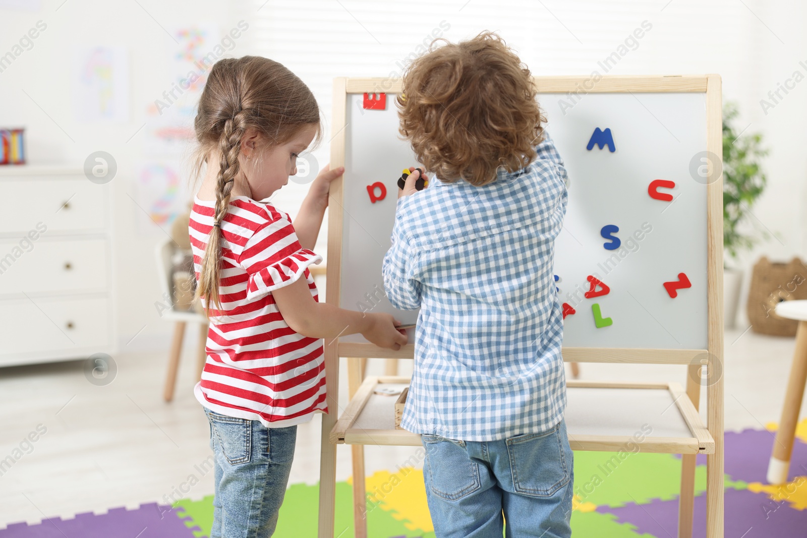 Photo of Cute little children learning alphabet with magnetic letters on board in kindergarten