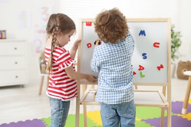 Photo of Cute little children learning alphabet with magnetic letters on board in kindergarten