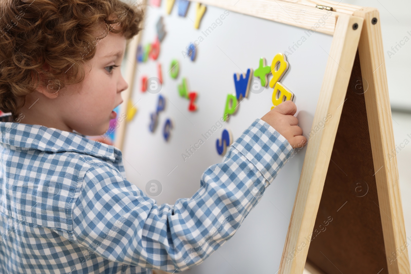 Photo of Cute little boy learning alphabet with magnetic letters on board in kindergarten