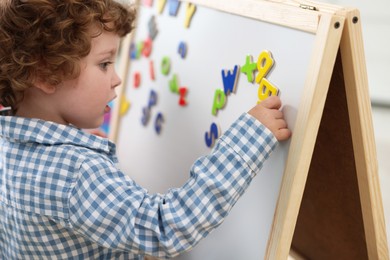 Photo of Cute little boy learning alphabet with magnetic letters on board in kindergarten