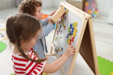 Little children learning alphabet with magnetic letters on board in kindergarten