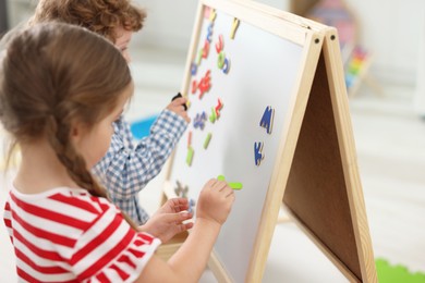 Little children learning alphabet with magnetic letters on board in kindergarten