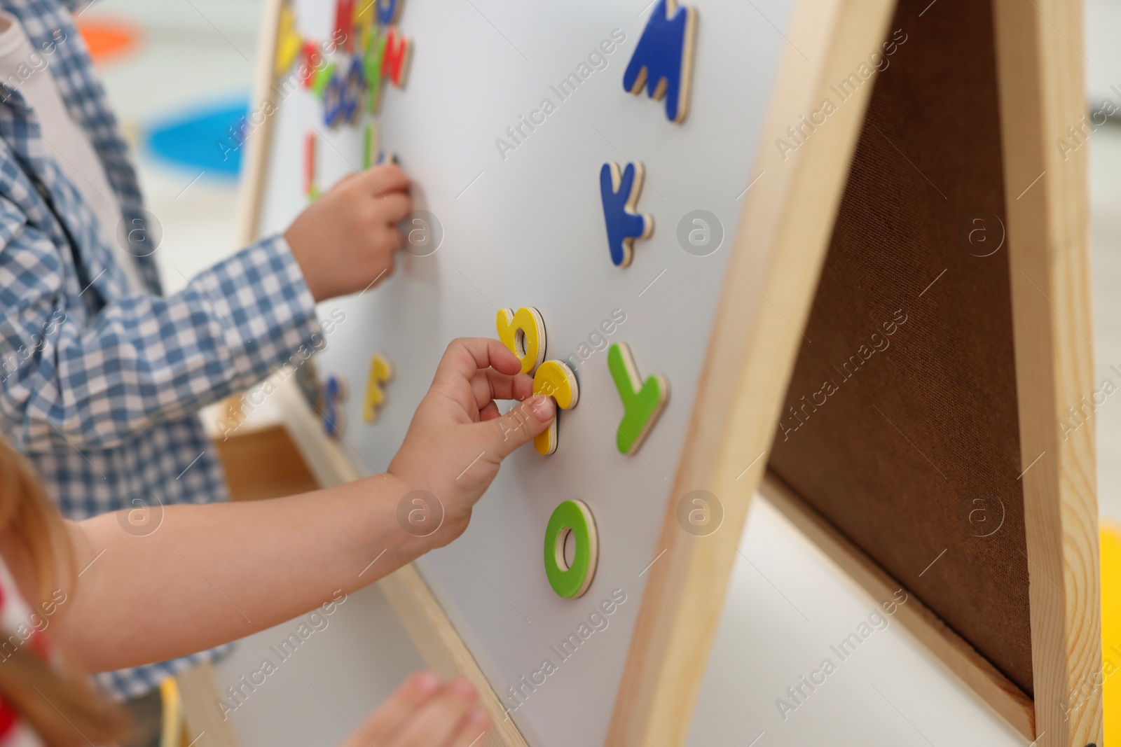 Photo of Little children learning alphabet with magnetic letters on board in kindergarten, closeup