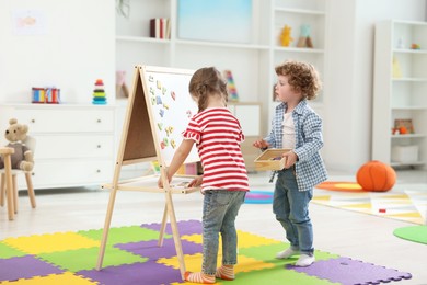 Photo of Little children learning alphabet with magnetic letters on board in kindergarten