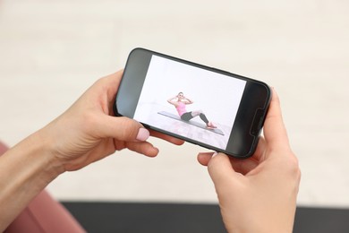 Photo of Online fitness trainer. Woman watching tutorial on smartphone indoors, closeup