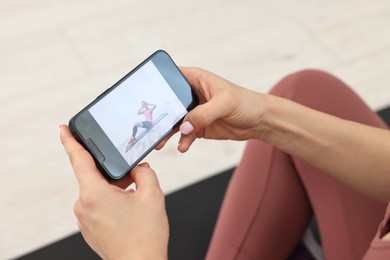 Photo of Online fitness trainer. Woman watching tutorial on smartphone indoors, closeup