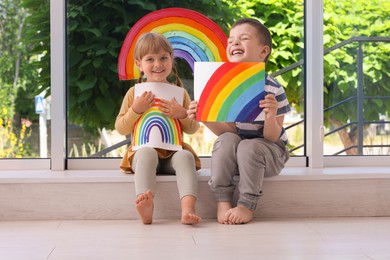 Children with pictures of rainbow near window indoors