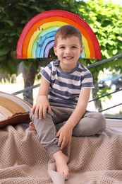 Happy little boy near rainbow painting on window indoors