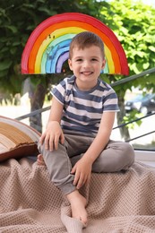 Photo of Happy little boy near rainbow painting on window indoors