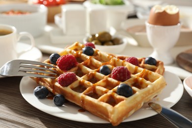 Photo of Tasty breakfast. Belgian waffles with berries, caramel sauce and cutlery on wooden table