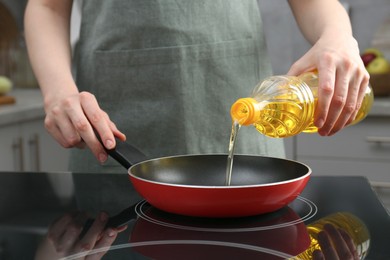 Photo of Vegetable fats. Woman pouring oil into frying pan on stove in kitchen, closeup