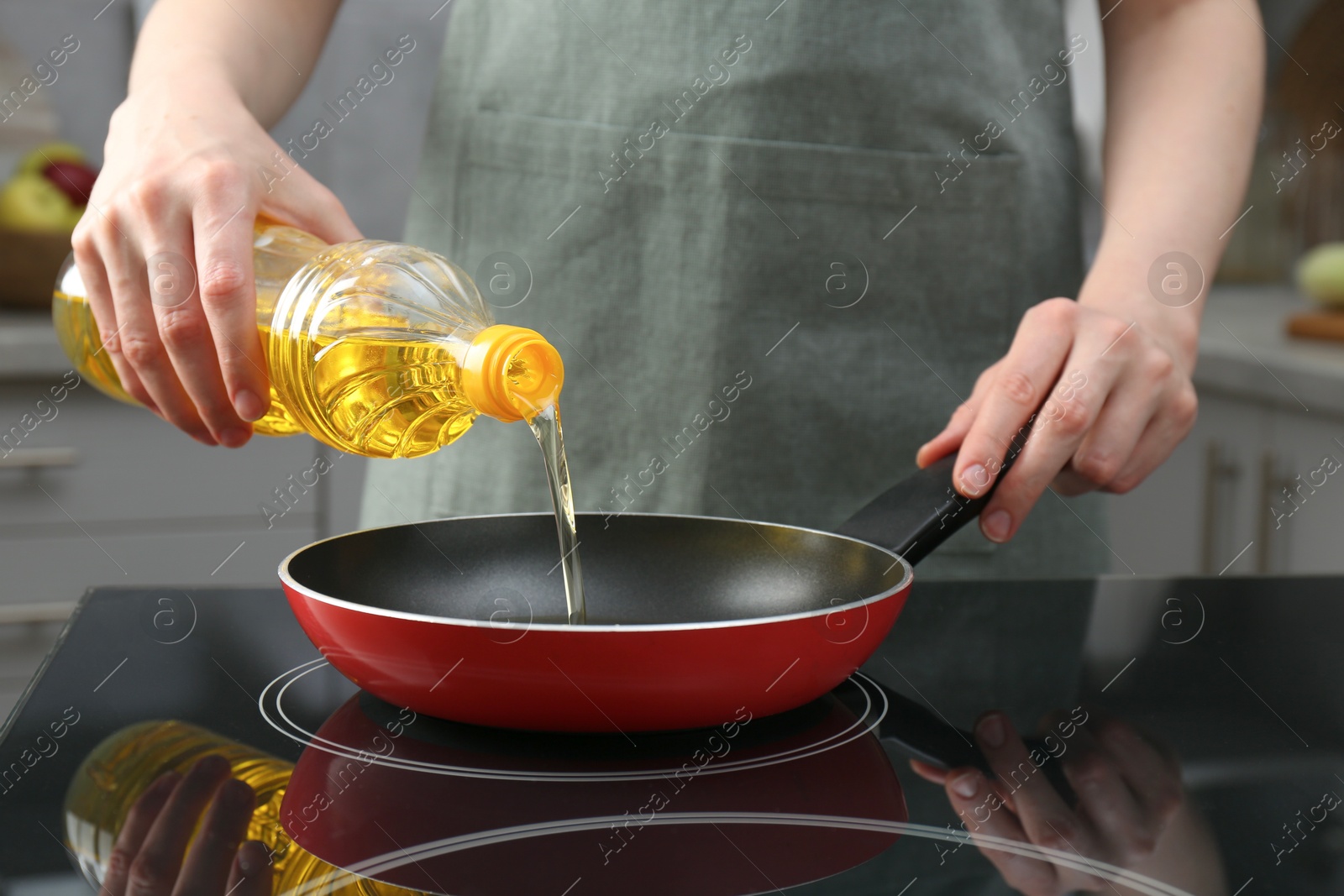 Photo of Vegetable fats. Woman pouring oil into frying pan on stove in kitchen, closeup