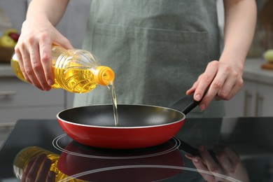 Photo of Vegetable fats. Woman pouring oil into frying pan on stove in kitchen, closeup