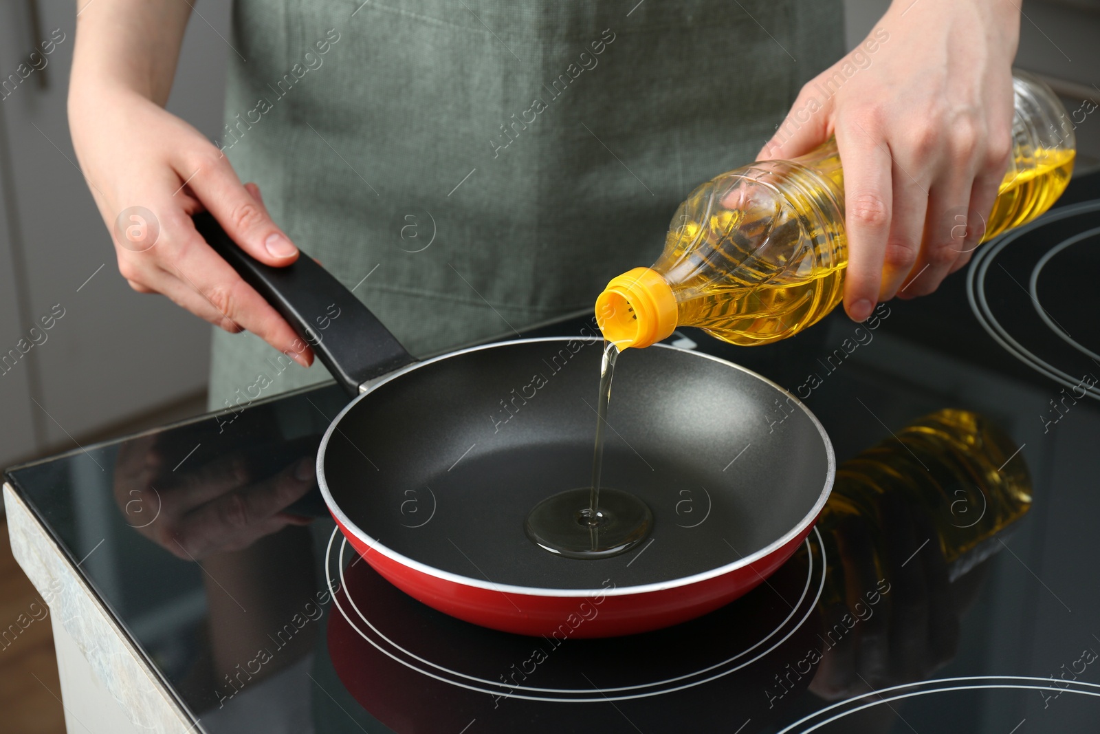 Photo of Vegetable fats. Woman pouring oil into frying pan on cooktop in kitchen, closeup