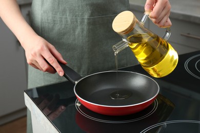 Photo of Vegetable fats. Woman pouring oil into frying pan on cooktop in kitchen, closeup