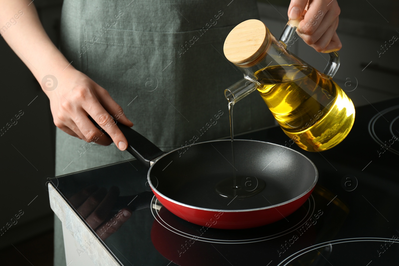 Photo of Vegetable fats. Woman pouring oil into frying pan on cooktop in kitchen, closeup