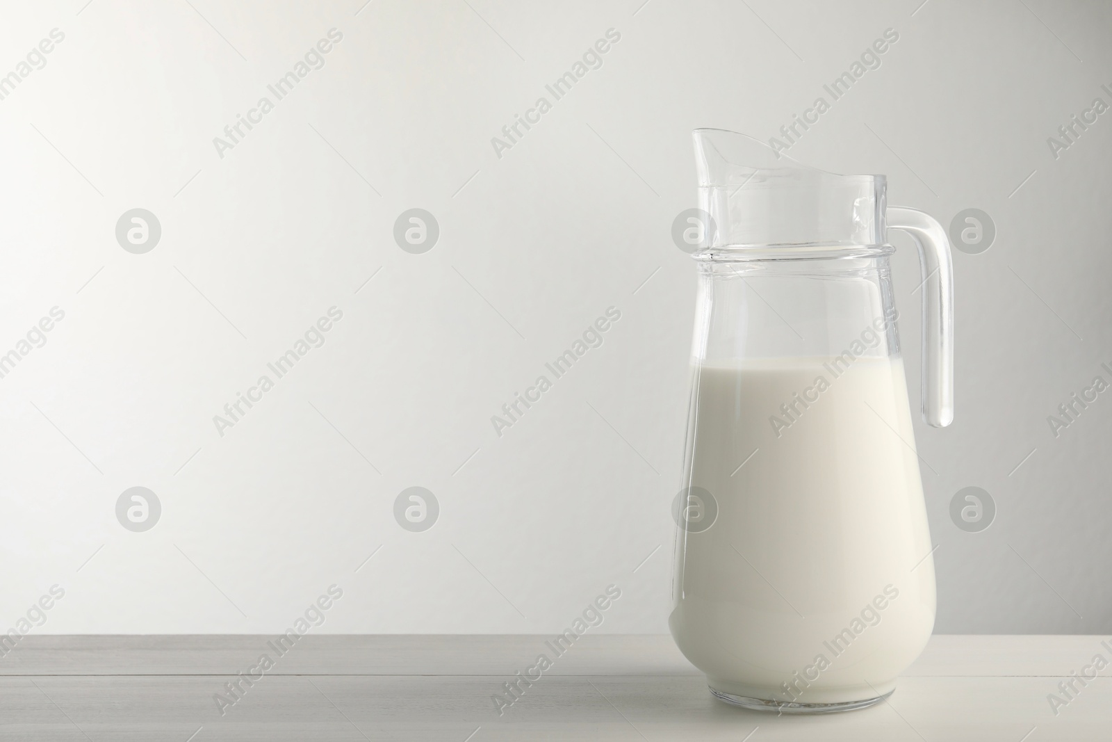 Photo of Glass jug with fresh milk on light wooden table. Space for text