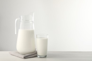 Photo of Jug and glass with fresh milk on light wooden table. Space for text