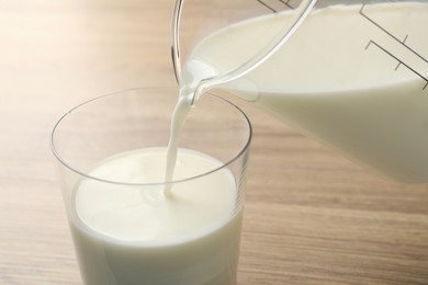 Pouring fresh milk from jug into glass at wooden table, closeup