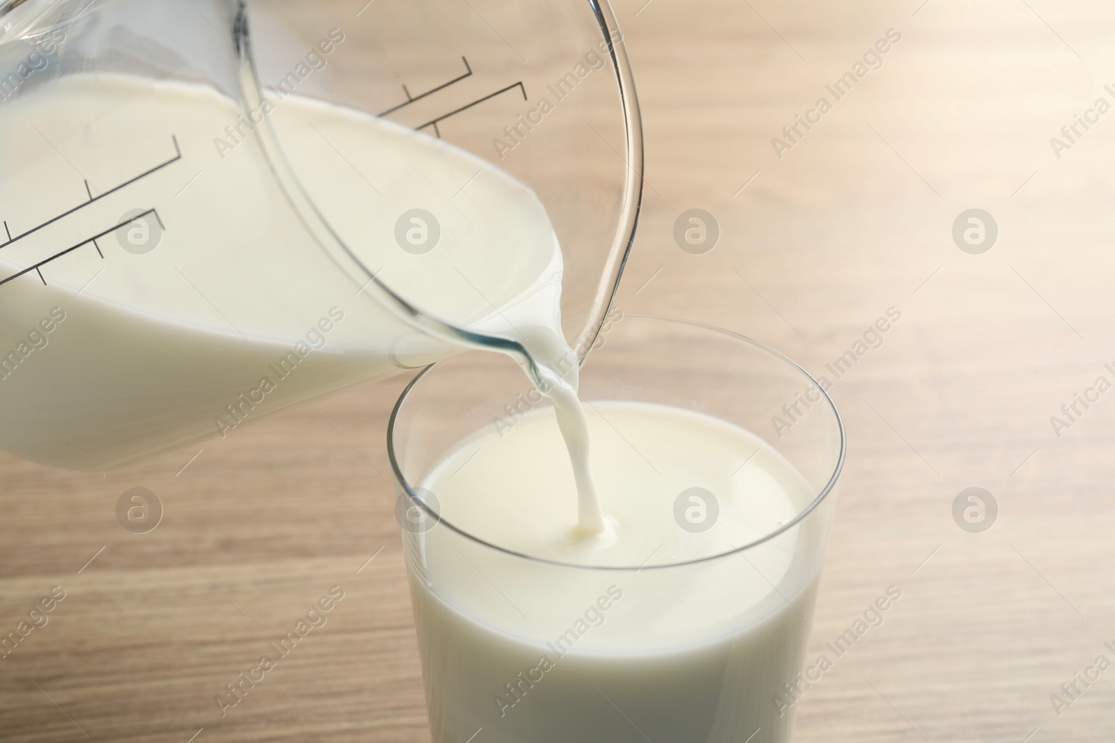 Photo of Pouring fresh milk from jug into glass at wooden table, closeup