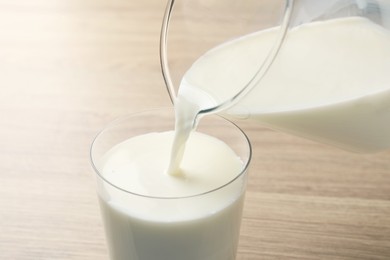 Photo of Pouring fresh milk from jug into glass at wooden table, closeup