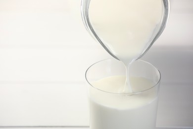 Photo of Pouring fresh milk from jug into glass at white table, closeup. Space for text