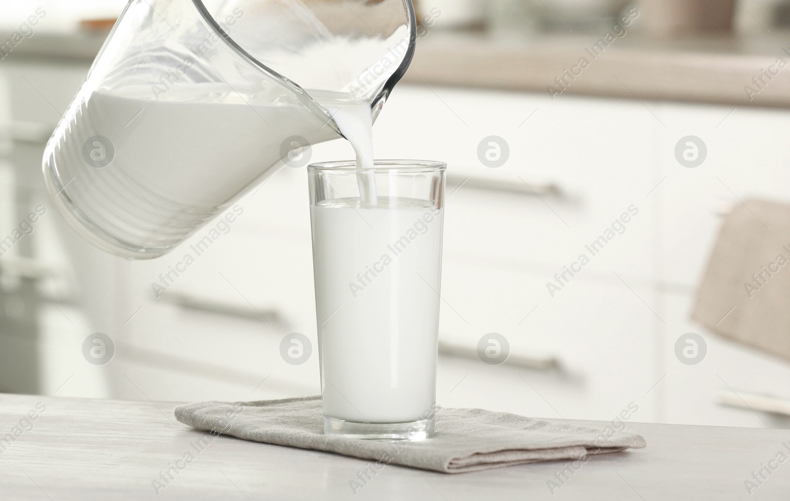 Photo of Pouring fresh milk from jug into glass at light wooden table in kitchen, closeup