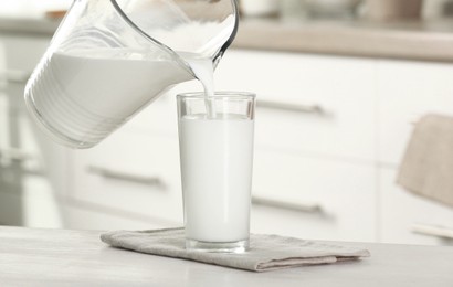 Pouring fresh milk from jug into glass at light wooden table in kitchen, closeup