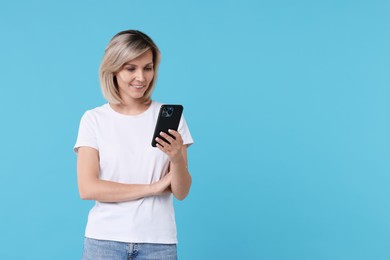 Happy woman with phone on light blue background, space for text