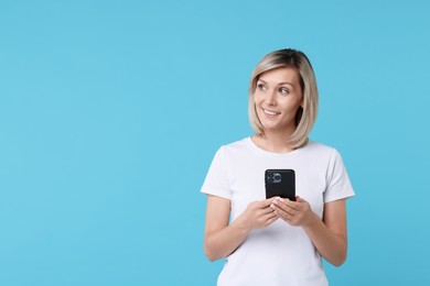 Happy woman with phone on light blue background, space for text