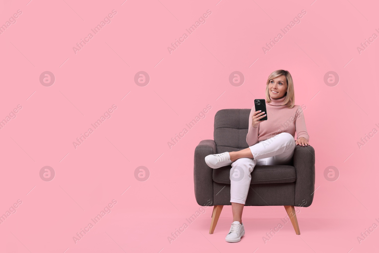 Photo of Happy woman with phone on armchair against pink background, space for text