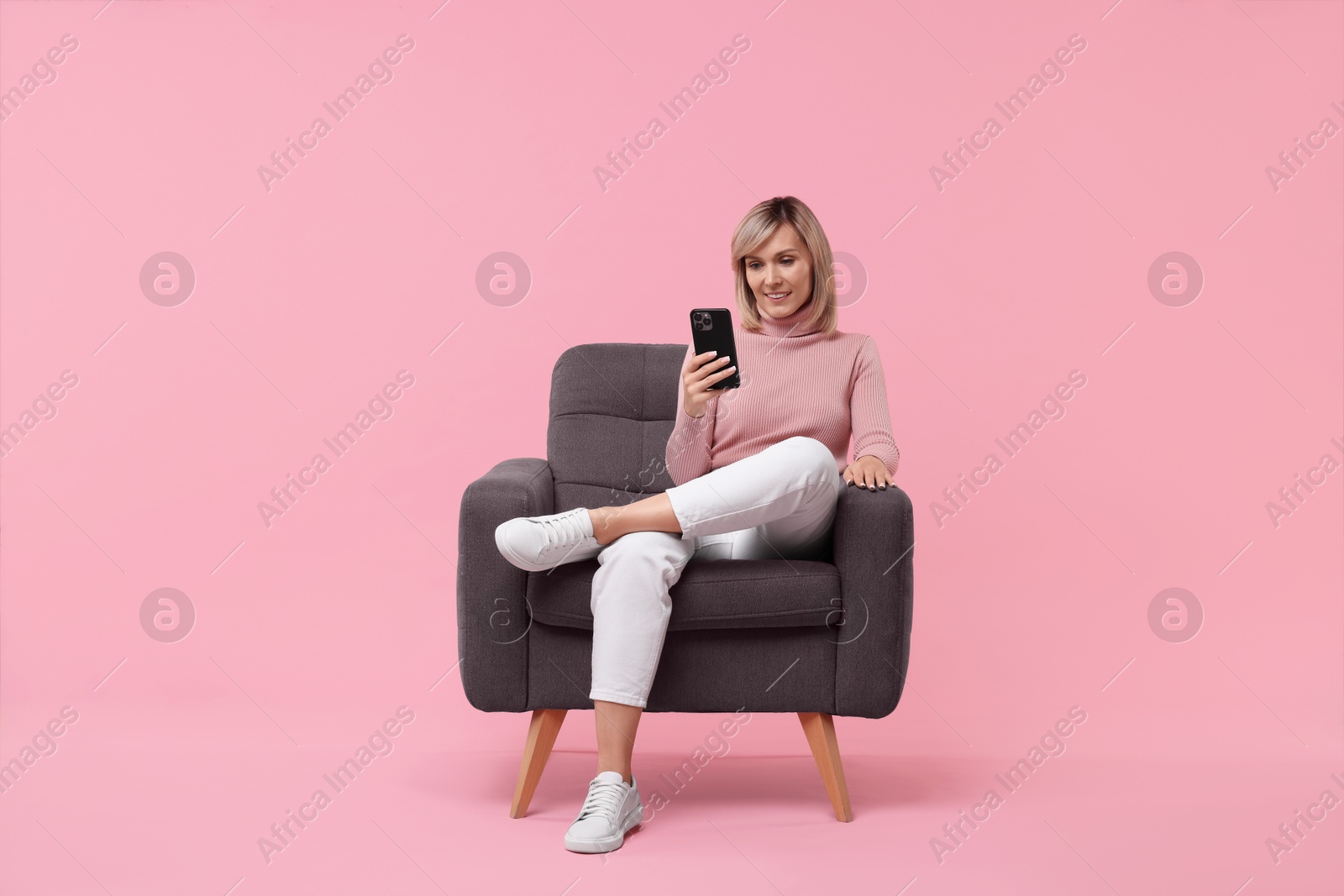 Photo of Happy woman with phone on armchair against pink background