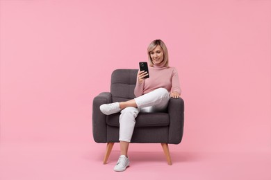 Happy woman with phone on armchair against pink background