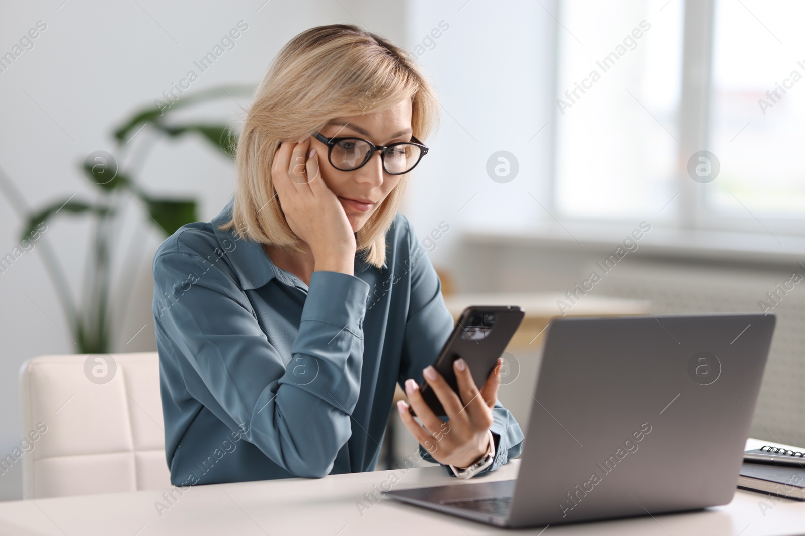 Photo of Woman using mobile phone at white table indoors