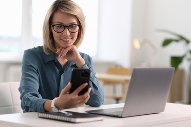 Happy woman using mobile phone at white table indoors