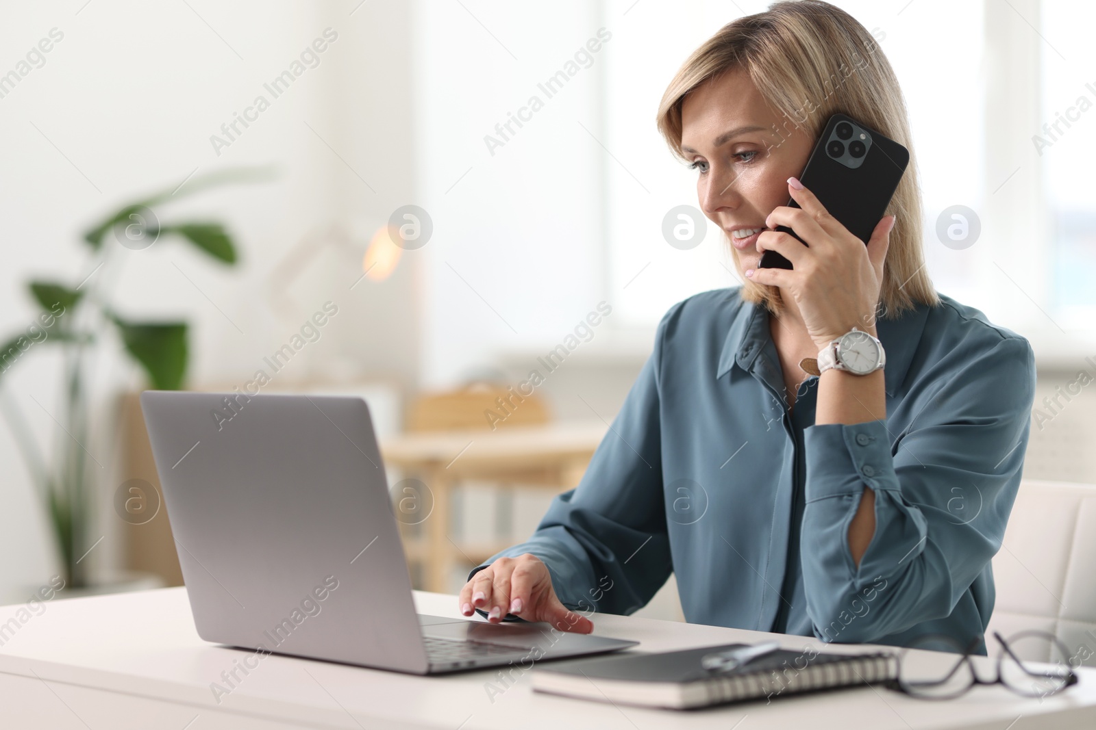 Photo of Happy woman using mobile phone at white table indoors